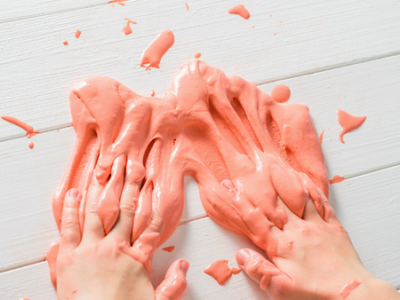 Child smears on a wooden table orange slime. Toy antistress. Toy for the development of hand motor skills.の写真素材