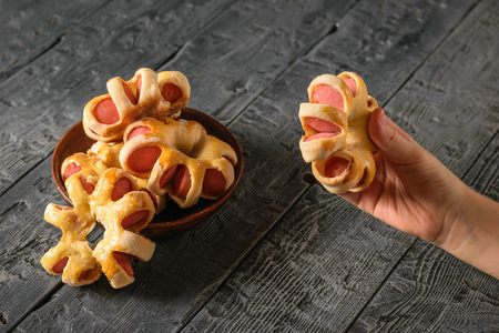The child takes a hand homemade sausage in the shape of an asterisk from the bowl. Tasty meat snack made of dough and sausages.の写真素材