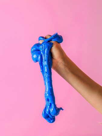 An blue slime flows down from the baby's hand on a pink background. Toy antistress. Toy for the...