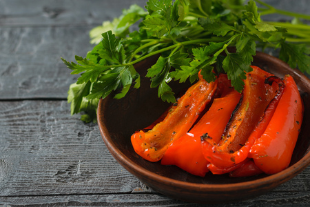 Pieces of red baked bell pepper in a bowl on a wooden table. Vegetarian dish. Natural plant food. The view from the top. Flat lay.の写真素材