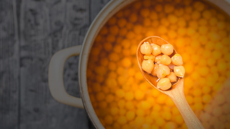Boiled chickpeas in a wooden spoon on the background of the table with a saucepan. Vegetarian...