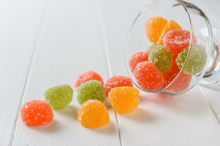 Pieces of colorful marmalade poured from a glass bowl on a white table. Delicious sweets made of jelly with sugar.の写真素材