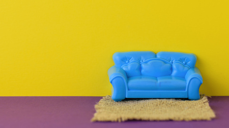 Beautiful blue sofa with a rug on the purple floor at the yellow wall. A sample of beautiful furniture for the house. Minimalist.の写真素材