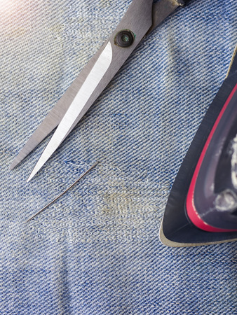 Scissors, needle and thread, and an iron on the ragged denim. Repair of jeans at home. The view from the top.の写真素材