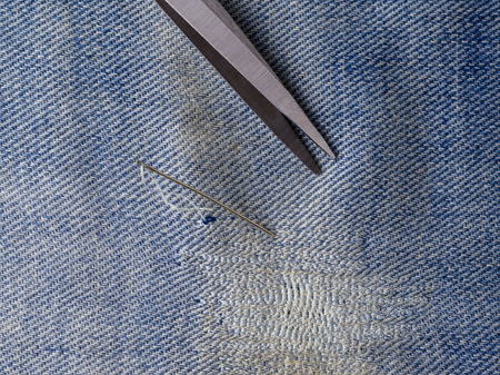 Scissors and needle on sewn denim blue fabric. Repair of jeans at home. The view from the top.