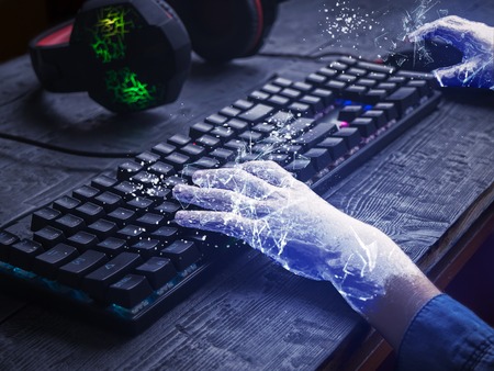 Child's hands covered with ice on the keyboard and gaming headphones on the wooden table. The...