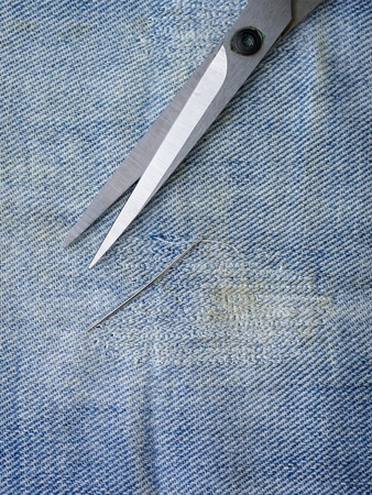 Scissors and a needle and thread on the torn denim. Repair of jeans at home. The view from the top.の写真素材
