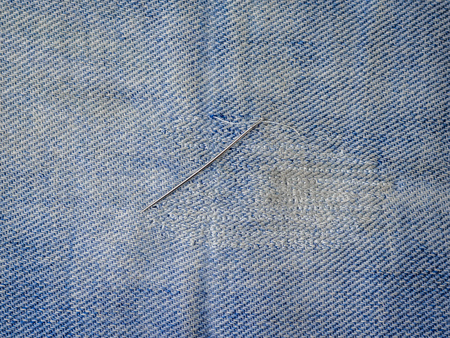 Iron needle with thread on the repaired denim. Repair of jeans at home. The view from the top.