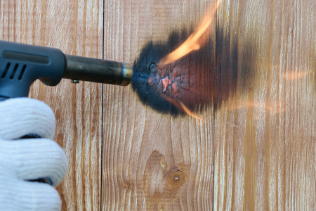 Hand in a glove with a burner performs firing of wooden panels. Treatment of the wooden surface...