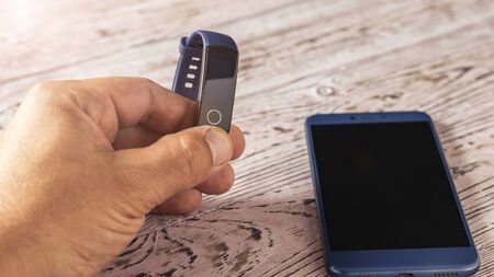 Blue smart bracelet in hand and blue smartphone on wooden table. Accessories to control sports....