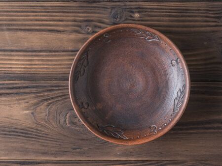 Clay bowl on a brown wooden table. The view from the top. Pottery for the kitchen. Flat lay.の写真素材