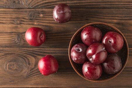 Bowl of plums and three plums on a wooden table. Fresh fruit harvest. The view from the top.の写真素材
