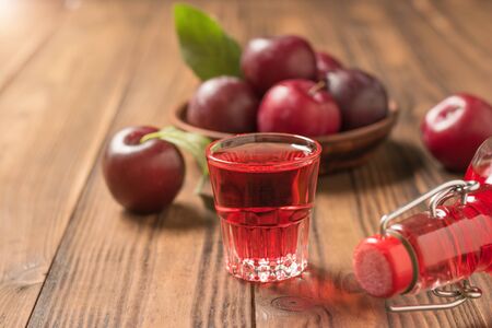 Plum liqueur in a glass and a bottle of fresh plums on a wooden table. Homemade alcoholic drink made from berries plum.の写真素材