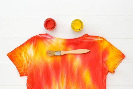 T-shirt painted in the style of tie dye and jars with red and yellow on a white table. Staining fabric in tie dye style.の写真素材