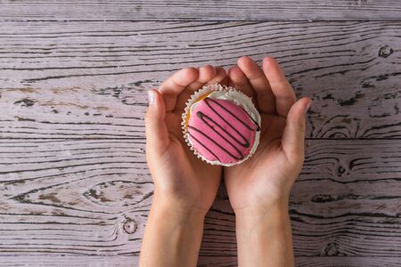 Fresh cupcake in the hands of a child on a wooden table. Freshly prepared homemade sweetness in the hands of a child.の写真素材