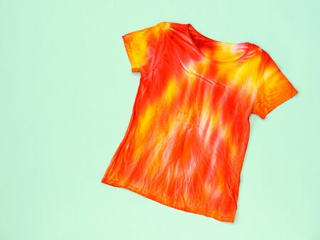 T-shirt in red and yellow in the style of tie dye on a light table. Flat lay. Staining fabric in tie dye style. Flat lay.の写真素材