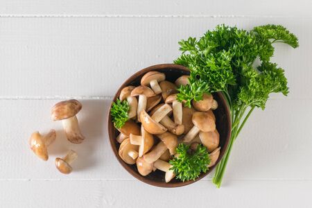Mushrooms in a clay bowl and on a white wooden table. Natural vegetarian cuisine. The view from the top.の写真素材