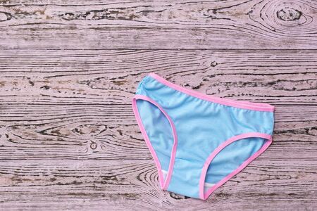 Women's panties are blue with a pink stripe on a wooden background. Fashionable concept. Beautiful lingerie. Fashionable concept. Beautiful lingerie. Flat lay.の写真素材