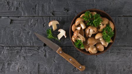 Knife with a bowl of fresh mushrooms on a rustic black wooden table. Natural vegetarian cuisine. The view from the top.の写真素材