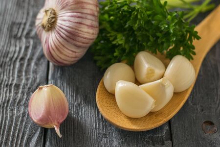 Peeled cloves of garlic in a wooden spoon and a whole garlic on a black wooden table. Healthy natural seasoning. Component of traditional medicine.の写真素材
