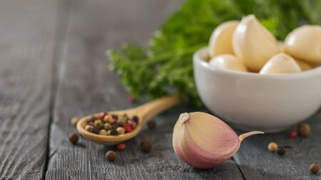 Garlic cloves and a wooden spoon with pepper on a wooden table. Healthy natural seasoning. Component of traditional medicine.の写真素材