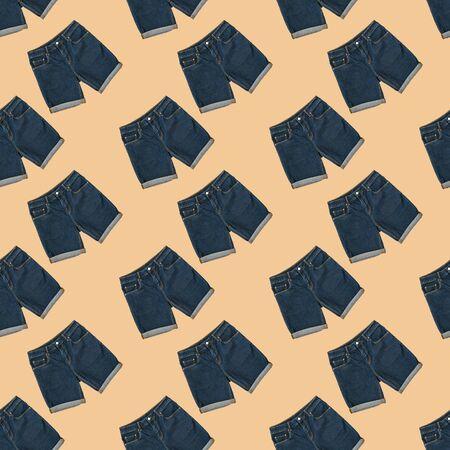 Seamless pattern of blue denim shorts on beige background. Fashionable unisex clothing. Summer denim...