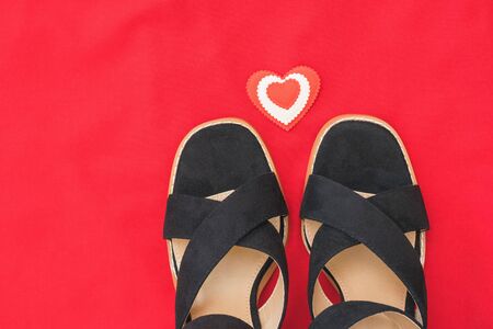Summer fashion black women's shoes on red fabric with red heart. Flat lay. The view from the top.