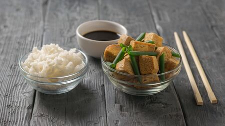 Grilled tofu cheese with green onions, rice and soy sauce on a wooden table. Grilled cheese appetizer.の写真素材