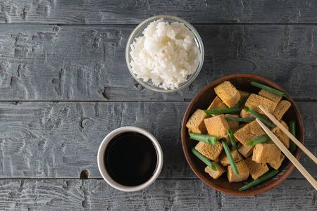 Grilled tofu cheese with green onions, rice and soy sauce on a wooden table. Grilled cheese appetizer. Flat lay.の写真素材
