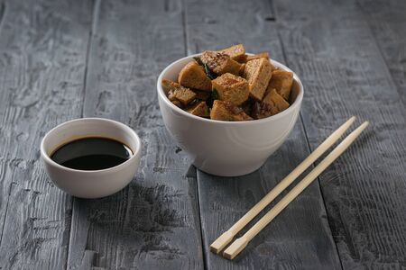 Two white cups of soy sauce and grilled tofu on a wooden table. Vegetarian Asian dish.の写真素材