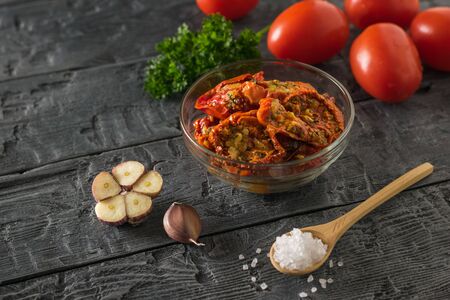 Glass bowl with roasted tomatoes on the background of fresh on the wooden table. Mediterranean tomato appetizer. Vegetarian food.の写真素材