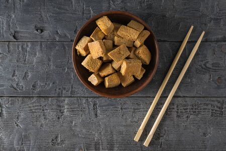Chopsticks and tofu cheese in a clay bowl on a wooden table. Vegetarian Asian dish.の写真素材