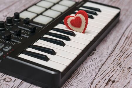 A red heart in the keys of a music mixer on a wooden table. Beautiful musical instrument.の写真素材