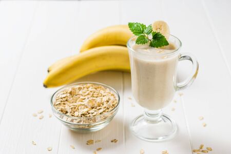 Smoothies in a glass, oatmeal and banana on a white table. Vegetarian smoothie. Sports nutrition.の写真素材