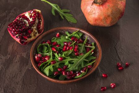 Arugula and pomegranate leaves in a clay bowl on a stone background. Diet vegetarian salad.の写真素材
