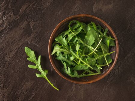 Fresh arugula leaves in a clay bowl on a stone background. Healthy plant-based diet. Vegetarian cuisine.の写真素材