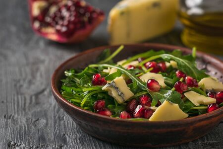 Salad of arugula, pomegranate and cheese with blue mold on a wooden table. Diet vegetarian salad.の写真素材