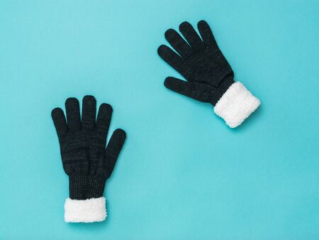Two knitted black women's gloves on a blue background. Winter accessories. Flat lay.