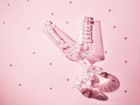 Two champagne glasses with streamers on a pink background with scattered sequins in the harsh light. Festive background with champagne glasses.の写真素材