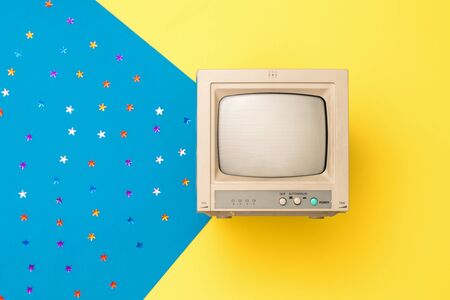 A small vintage monitor on a yellow background with a beam of blue background and sequins. Vintage electronics. The view from the top.の写真素材