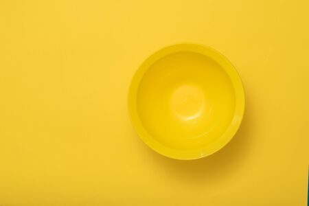 A large deep yellow bowl on a yellow background. Plastic utensils for the kitchen.の写真素材