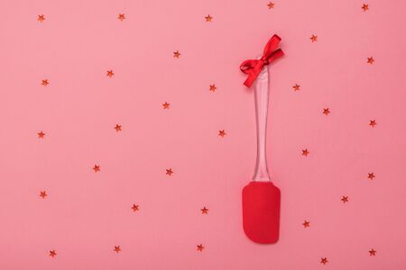 Bright red kitchen spatula decorated with red ribbon on pink background with stars. Kitchen tools on festive background. Flat lay.の写真素材