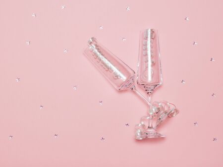 A pair of crystal glasses with legs on a bright background with sequins. Festive background with champagne glasses.の写真素材