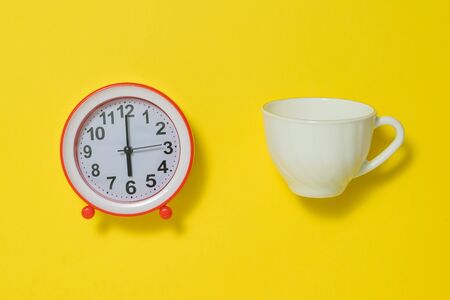 Coffee Cup and white analog alarm clock on yellow background. The concept of lifting the tone in the...
