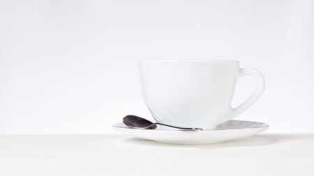 A white Cup for tea or coffee and a metal spoon on a white table on a gray background. Dishes for tea and coffee.の写真素材