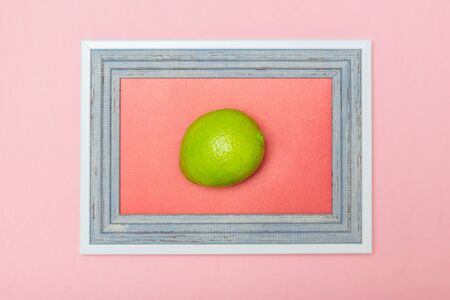 Lime in a wooden frame on a pink background. Citrus fruits for making a drink. Flat lay.