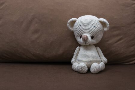 A small white knitted bear on a soft sofa. Beautiful knitted toy.