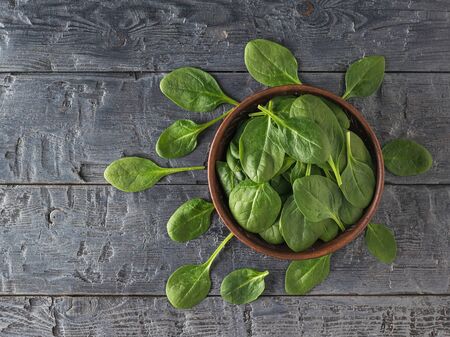 Fresh juicy spinach leaves in a clay plate and on a wooden table. Food for fitness. Vegetarian food....