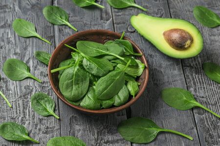 A bowl of spinach leaves and half an avocado on a wooden table. Ingredients for the drink and salad.の写真素材
