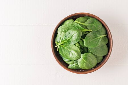 A clay bowl with spinach leaves on a white wooden table. Food for fitness. Vegetarian food. The view from the top.の写真素材